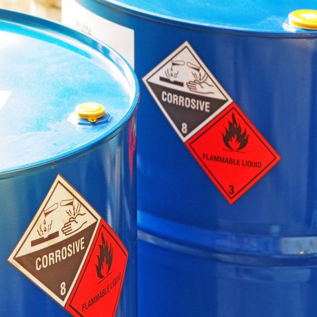 the close-up shot of blue color hazardous dangerous chemical barrels ,have warning labels of corrosive & flammable liquid in daylight on daytime.